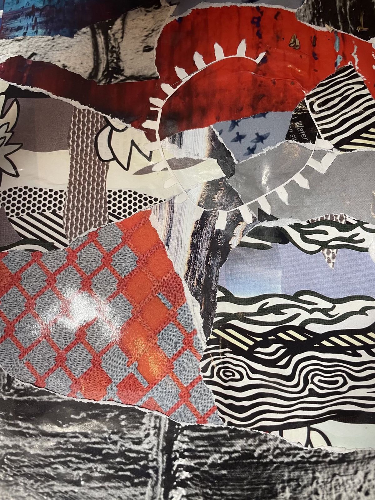 A mixed-media collage of torn paper pieces in red, black, white, and gray patterns layered over a brick-textured background.