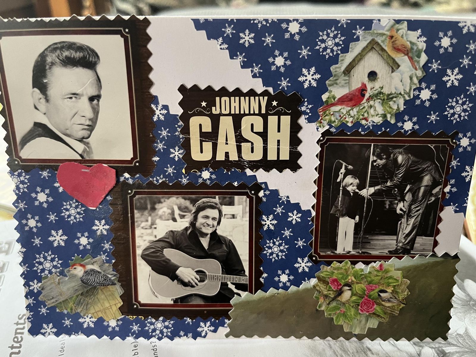A handmade greeting card made from upcycled junk-mail and magazine clippings: black-and-white Johnny Cash photos, cut-out birds, and a red heart on a snowflake-patterned blue background with zigzag pinked edges.