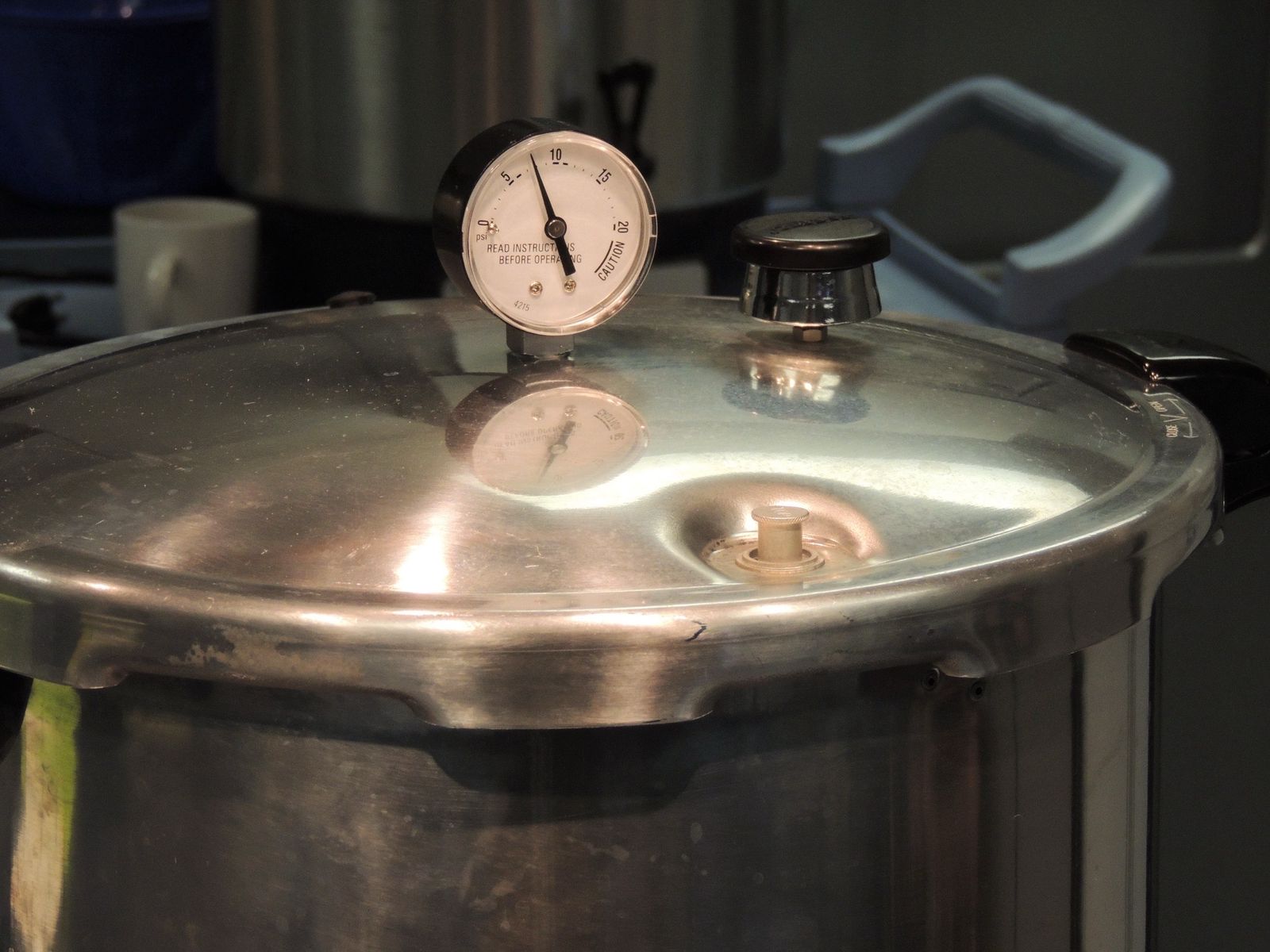 The lid of a stainless steel pressure canner, its dial gauge reading about 10 psi, sitting on a stove.