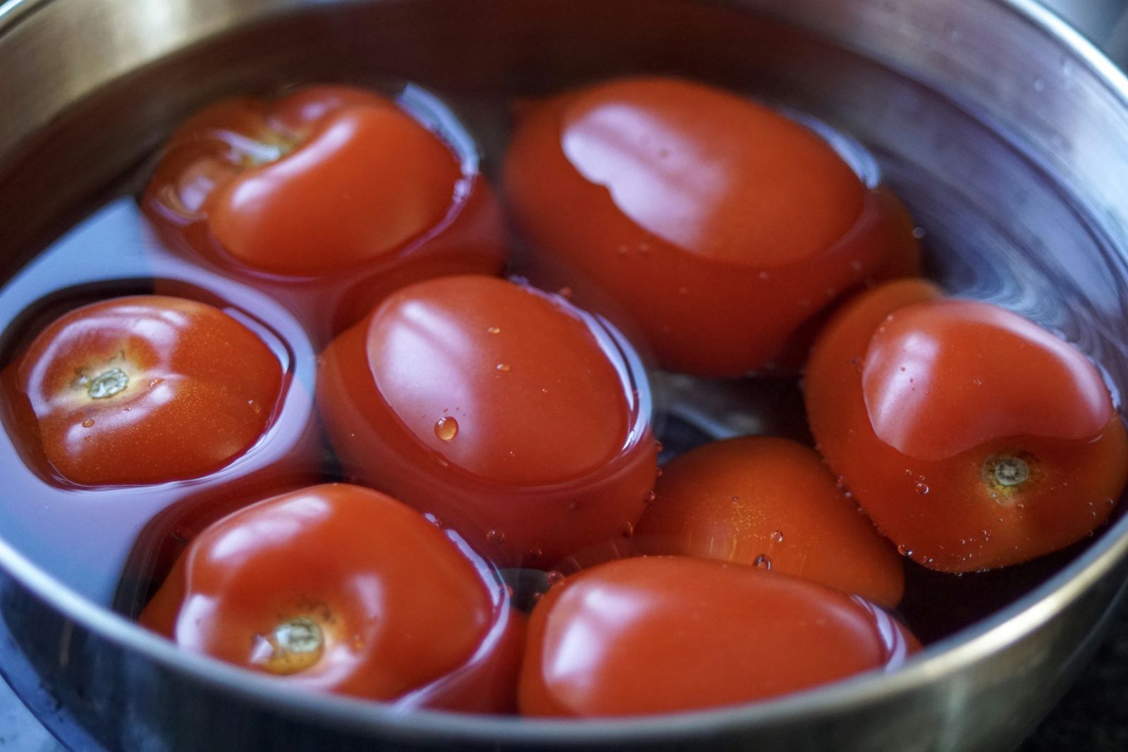 Whole red plum tomatoes sitting in a stainless steel pot of water, ready to be processed.